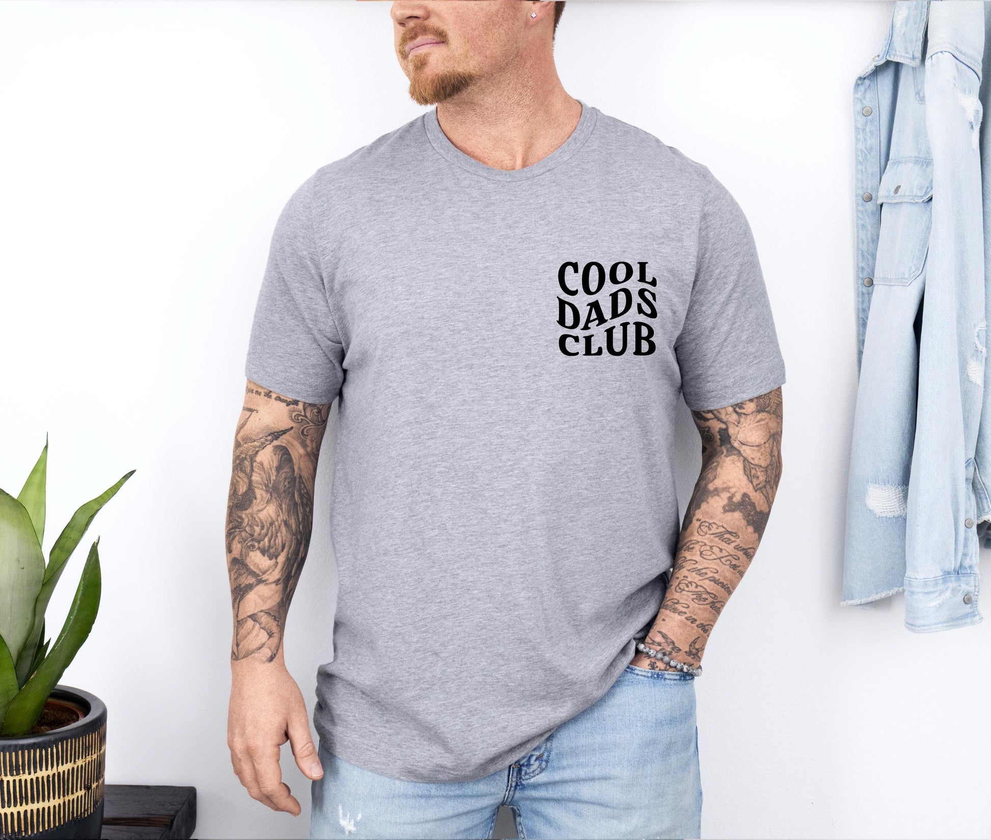 a man with a tattooed arm standing next to a plant